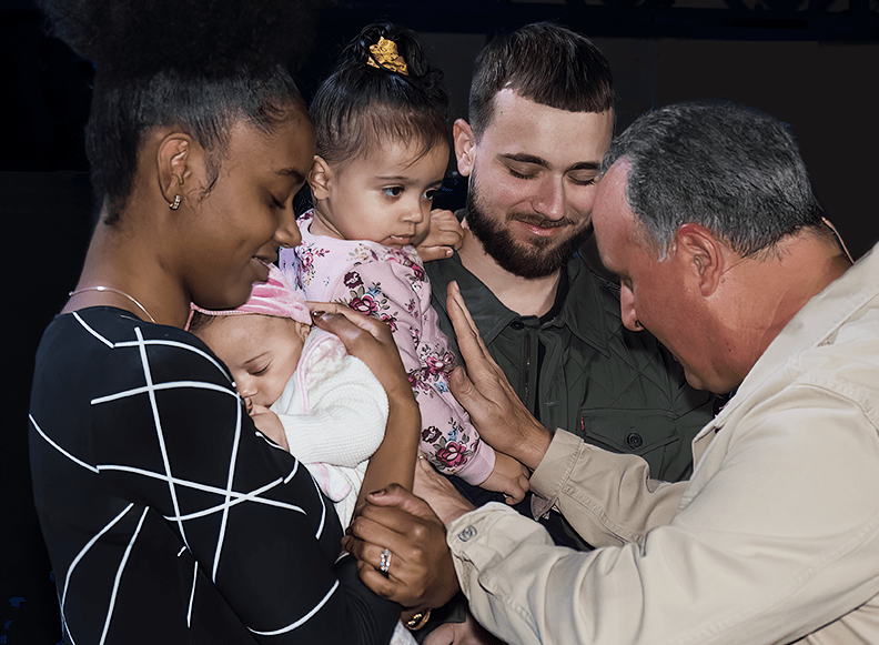Pastor John Nuzzo praying over a baby during a baby dedication